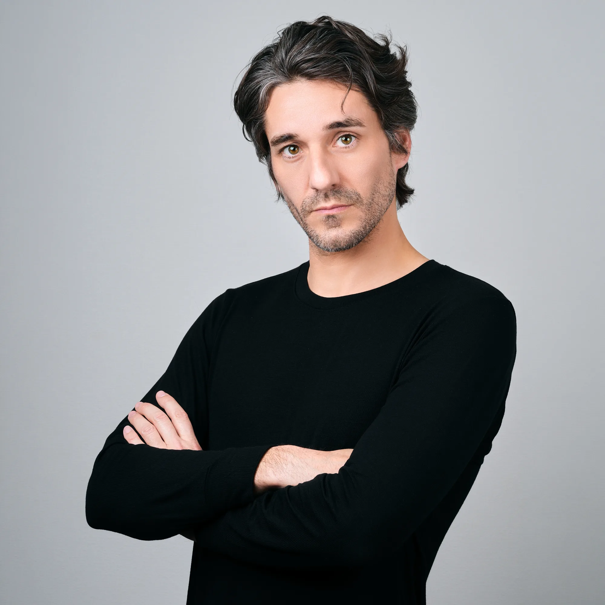 JG, photographer at JG Studio, arms crossed in a black long-sleeve top, photographed with studio strobes against a grey backdrop in Shibuya, Tokyo.